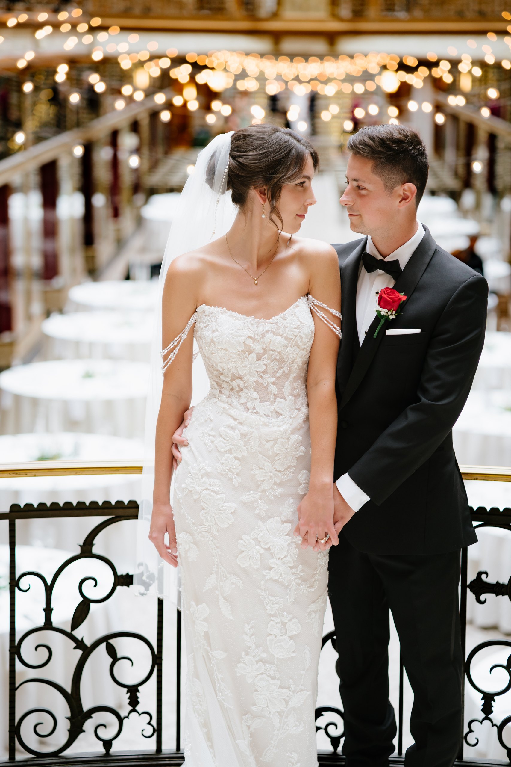 A bride and groom standing beneath reception lights