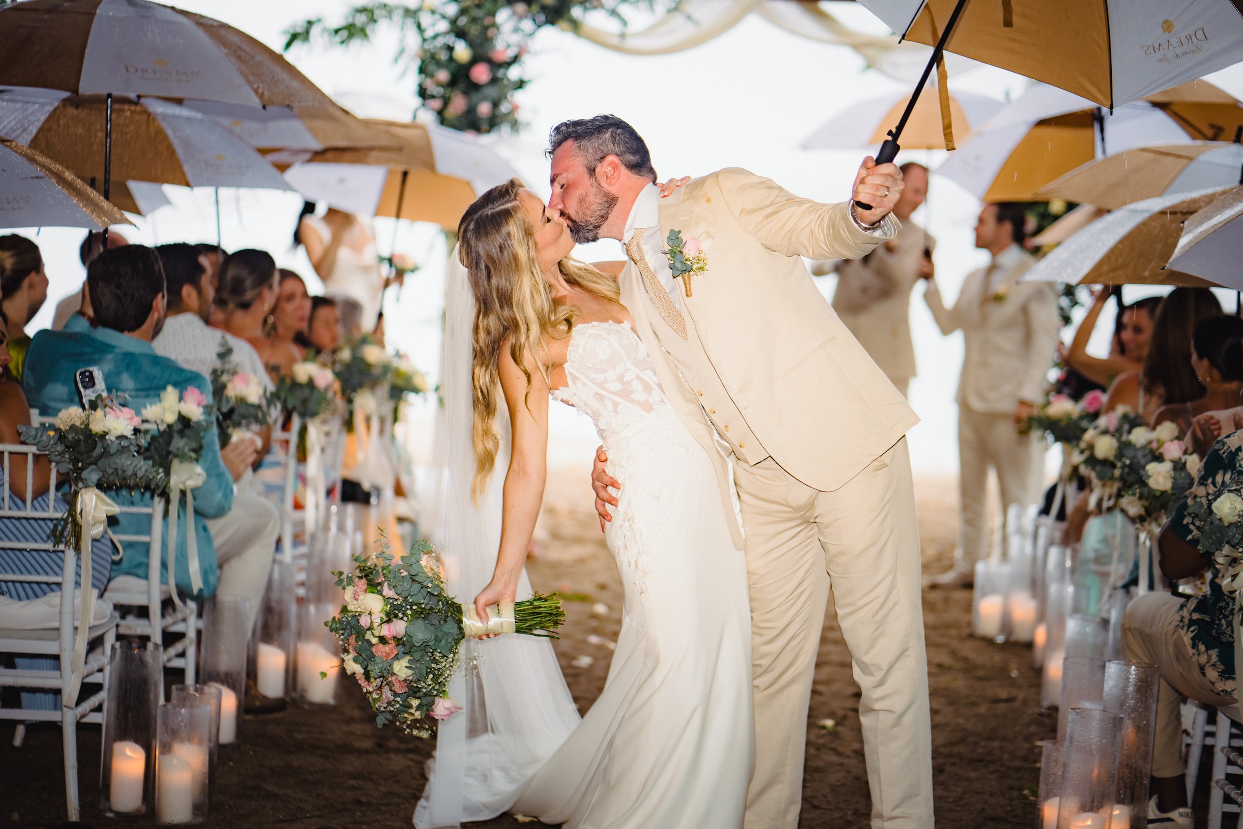 Newlyweds kissing beneath umbrellas at their ceremony